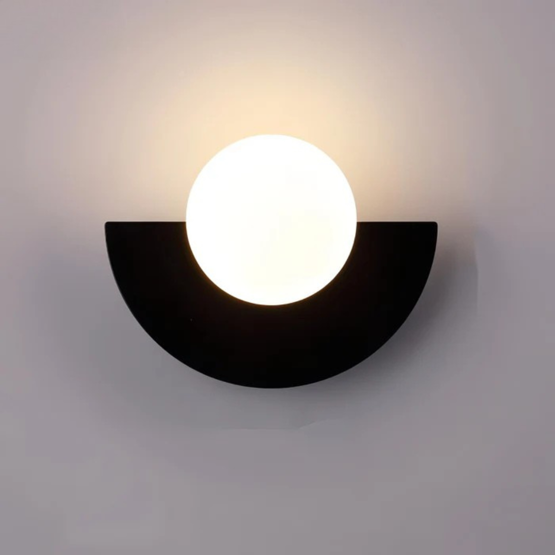 Lyca half moon globe wall sconce in black, lit on a gray wall