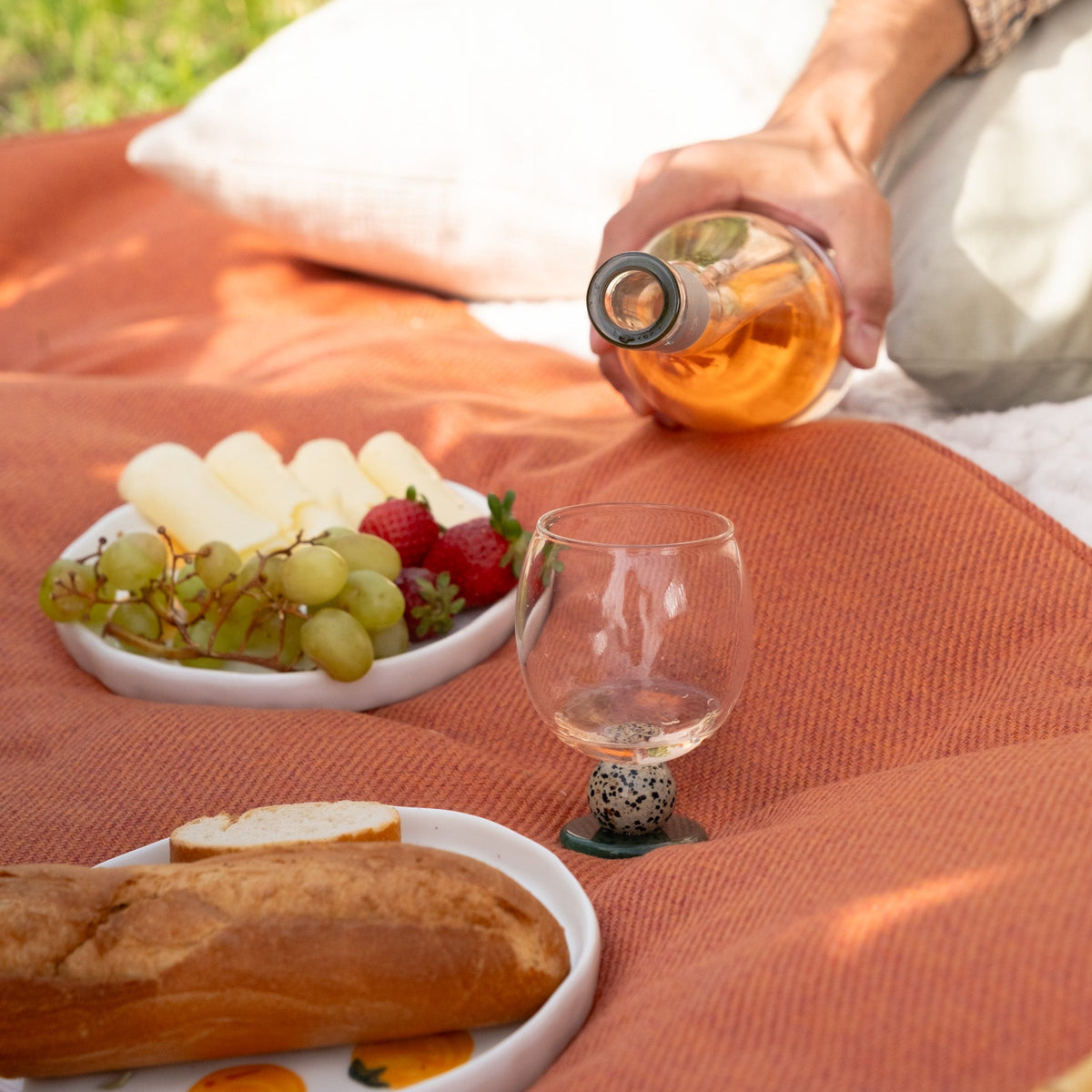 Stone base glass next to bread and grapes on a picnic cloth