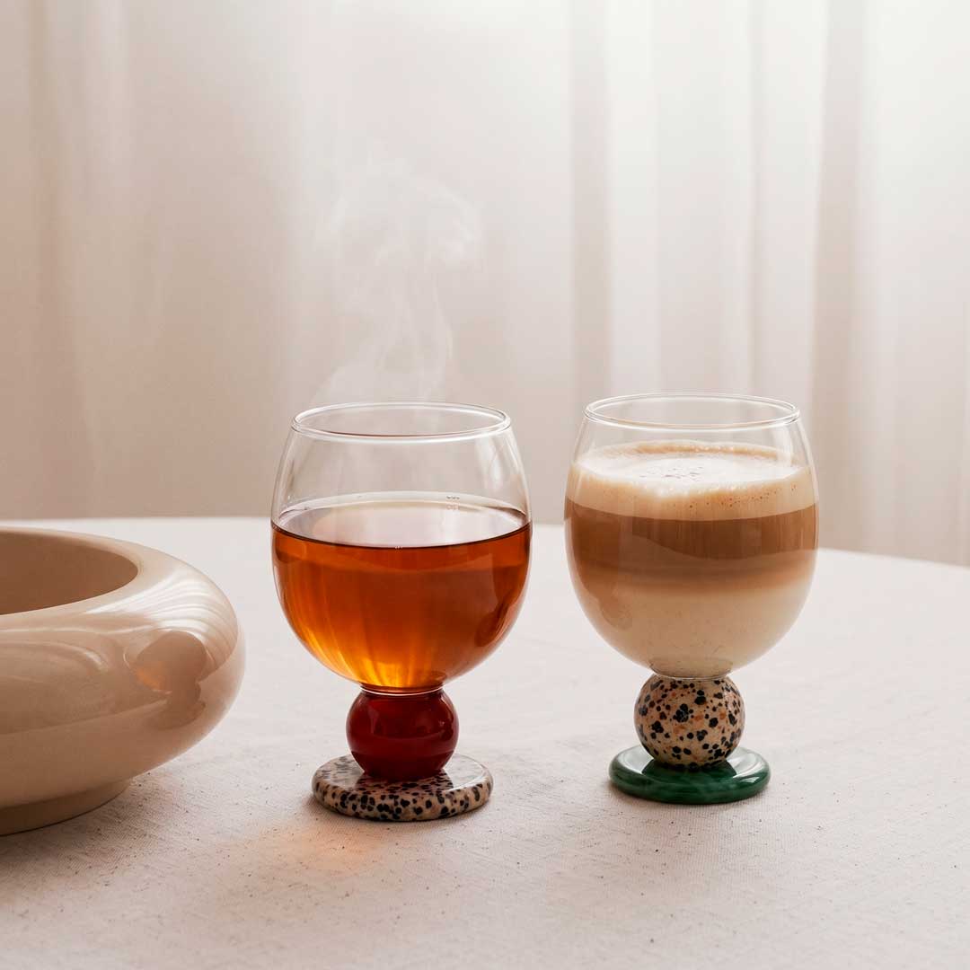 Two stone base glasses with tea and coffee on a white table