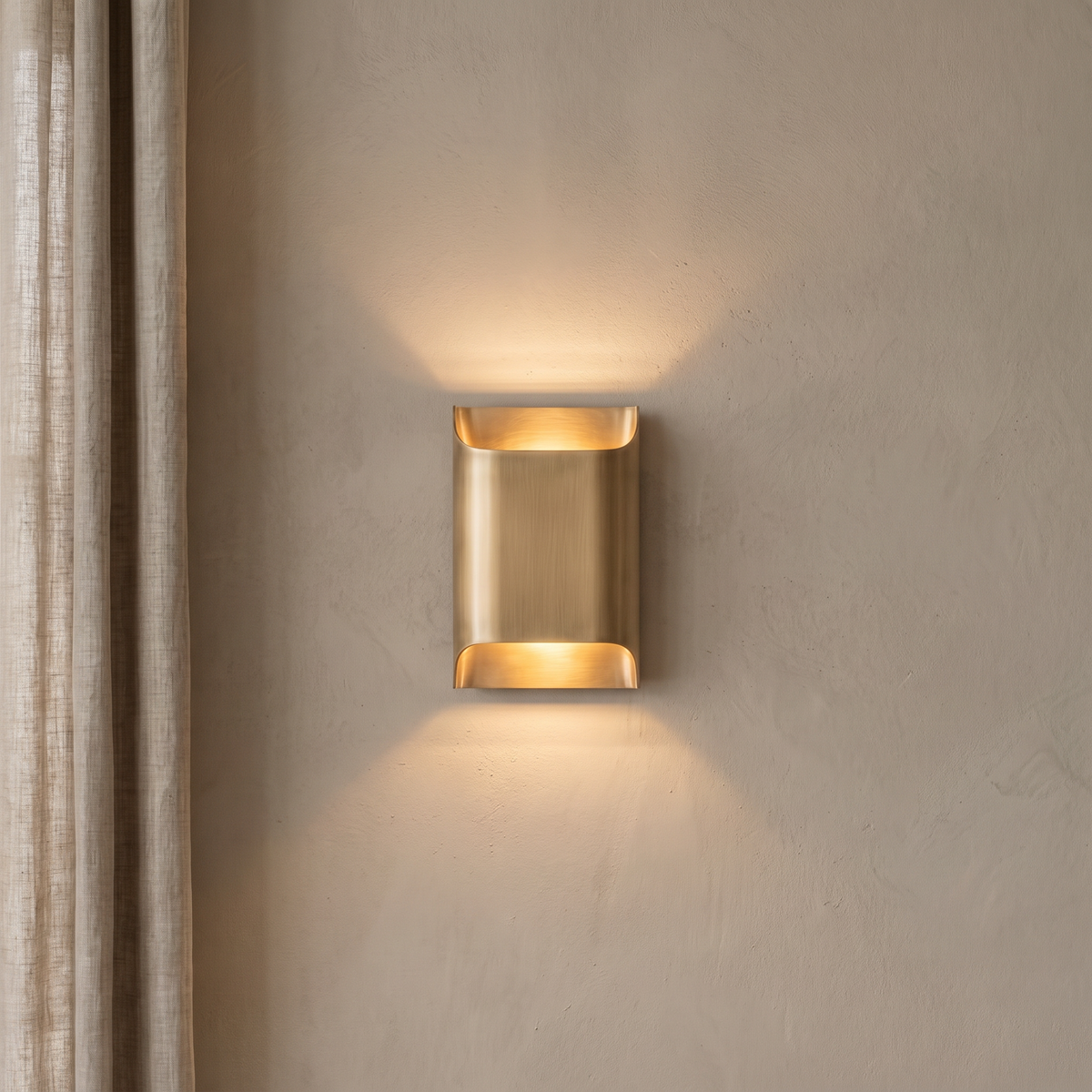 Tall brass wall sconce lit on a beige plaster wall