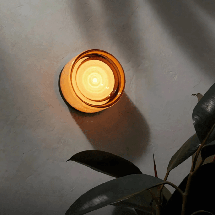 Orange Hera glass wall sconce glowing on a gray plaster wall