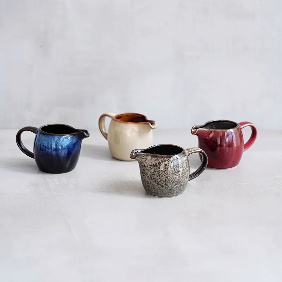 Four small kiln glazed jugs in blue, cream, gray and red