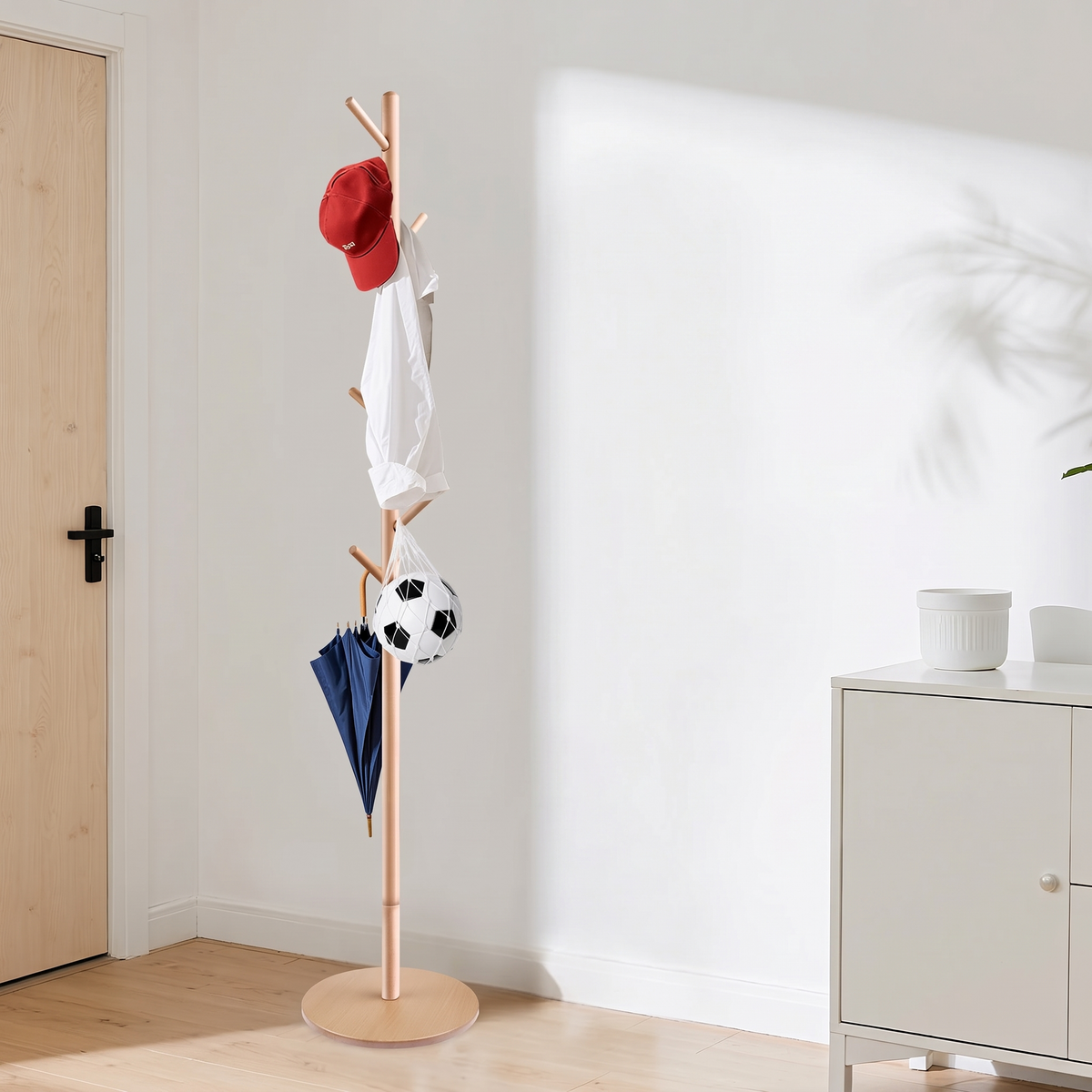 Natural coat stand by a door holding a cap, a shirt, an umbrella and a ball