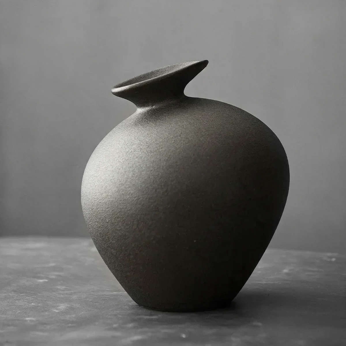 Matte black ceramic bud vase jar with a flared lip on a gray table