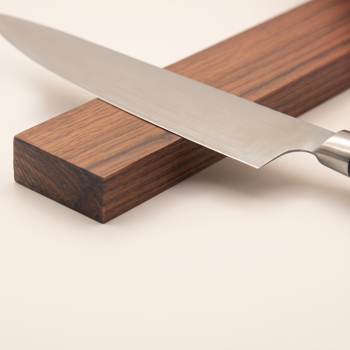 Chef knife held against the walnut grain of a magnetic knife strip