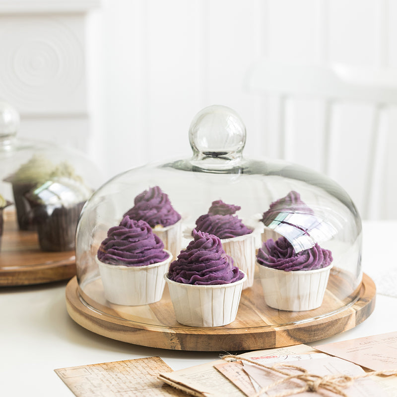 Purple cupcakes under a glass dome on a wood cake plate