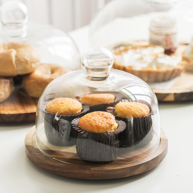 Muffins under a glass dome on a wood cake plate