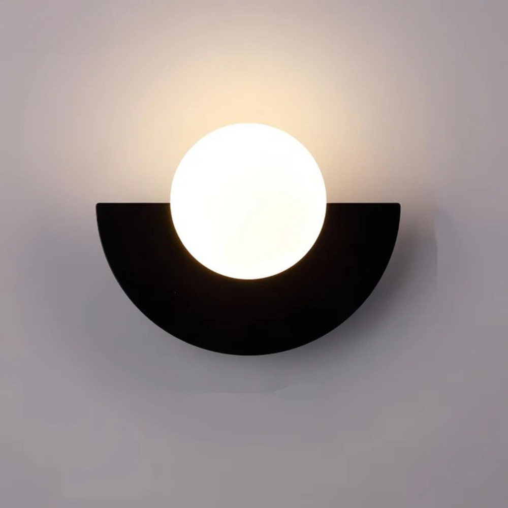 Lyca half moon globe wall sconce in black, lit on a gray wall