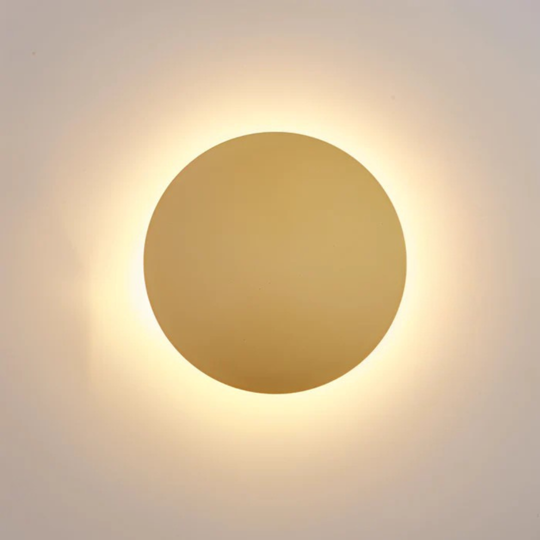 Hadro round LED wall light in gold, lit on a beige wall