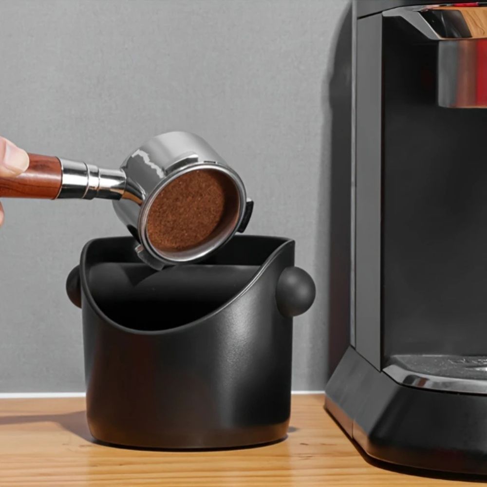 Knocking a used espresso puck into the black knock box beside a machine