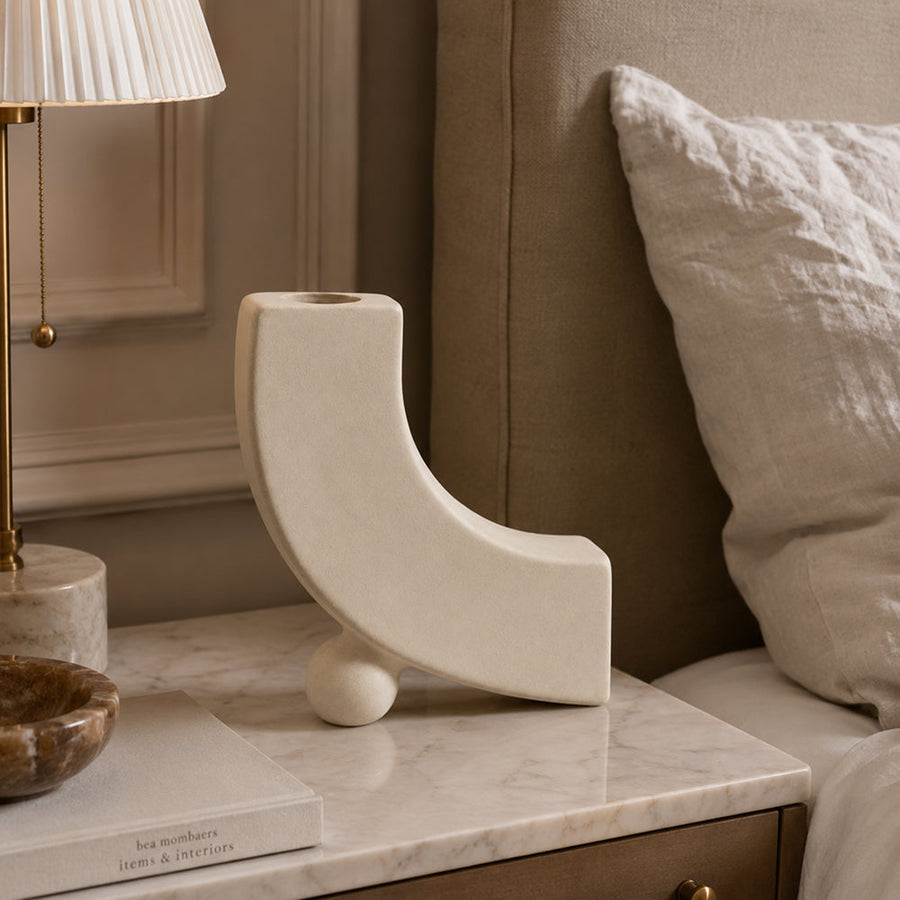 Matte unglazed ceramic arc vase with an open sweeping curve on a shelf