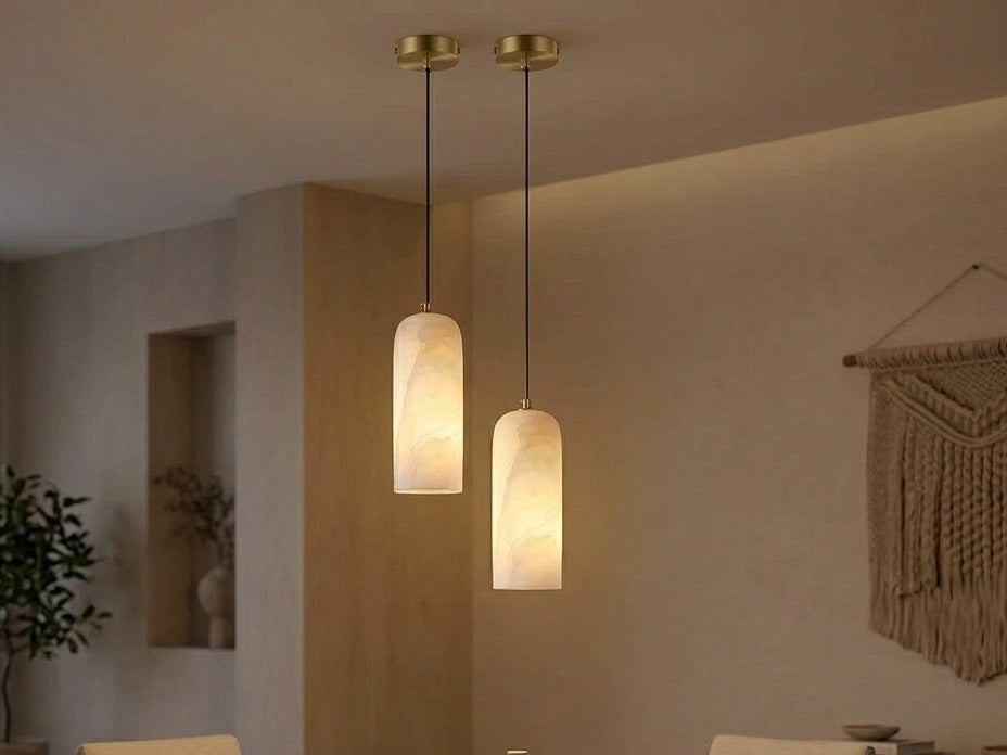 Two lit alabaster pendant lights with brass canopies hanging at staggered heights