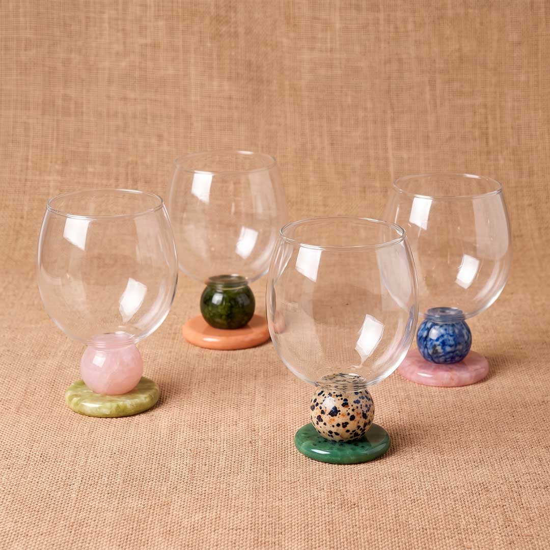 Five empty stone base glasses in different colors on a beige table