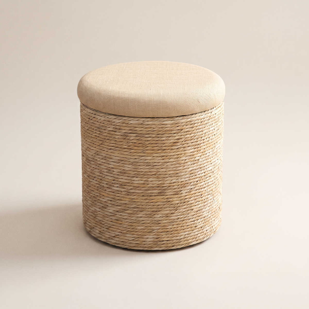 Round woven storage ottoman with a padded sand lid on a plain background