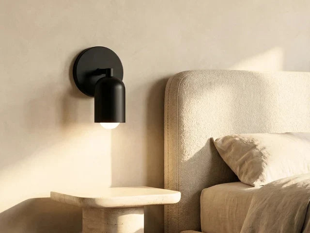 Black iron wall sconce lit above a stone nightstand next to a bed