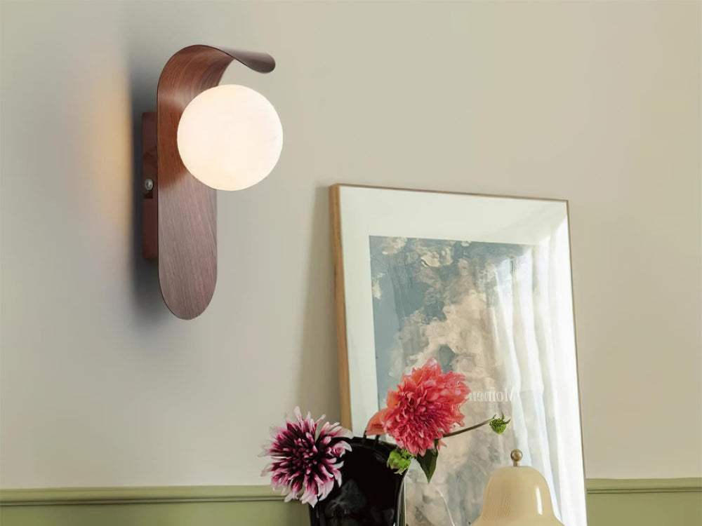 Carlyle wall lamp in walnut color lit above a wooden sideboard with flowers and a framed print
