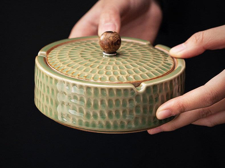 Green hammered ceramic ashtray with lid and wooden knob held in two hands