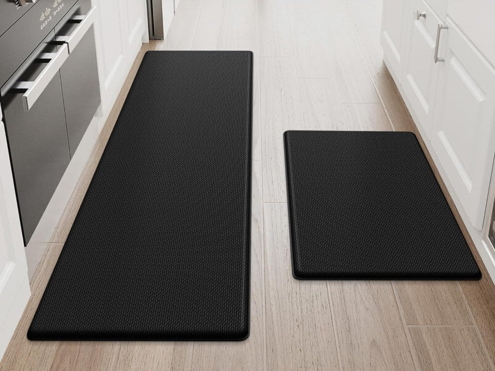 Two black anti-fatigue kitchen mats on a wood kitchen floor