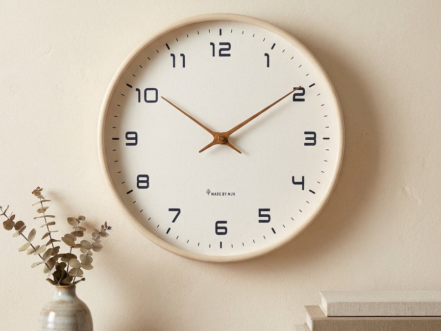 Cream wood wall clock with a white dial hanging above a shelf with a vase and books