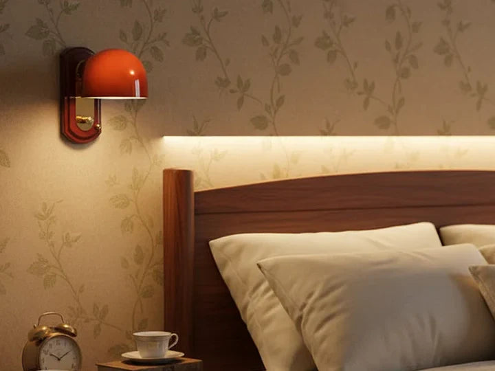 Red orange dome wall sconce lit above a nightstand beside a bed