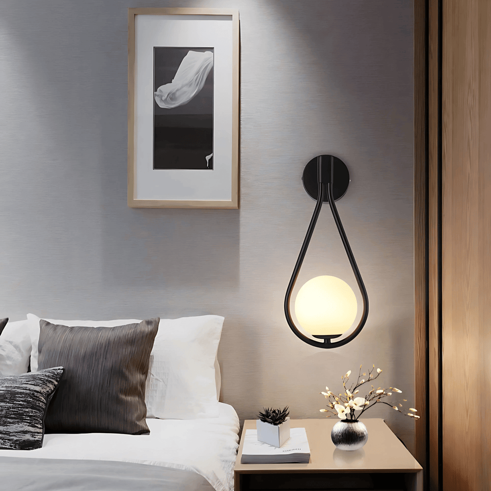 Black teardrop wall sconce above a nightstand beside the bed