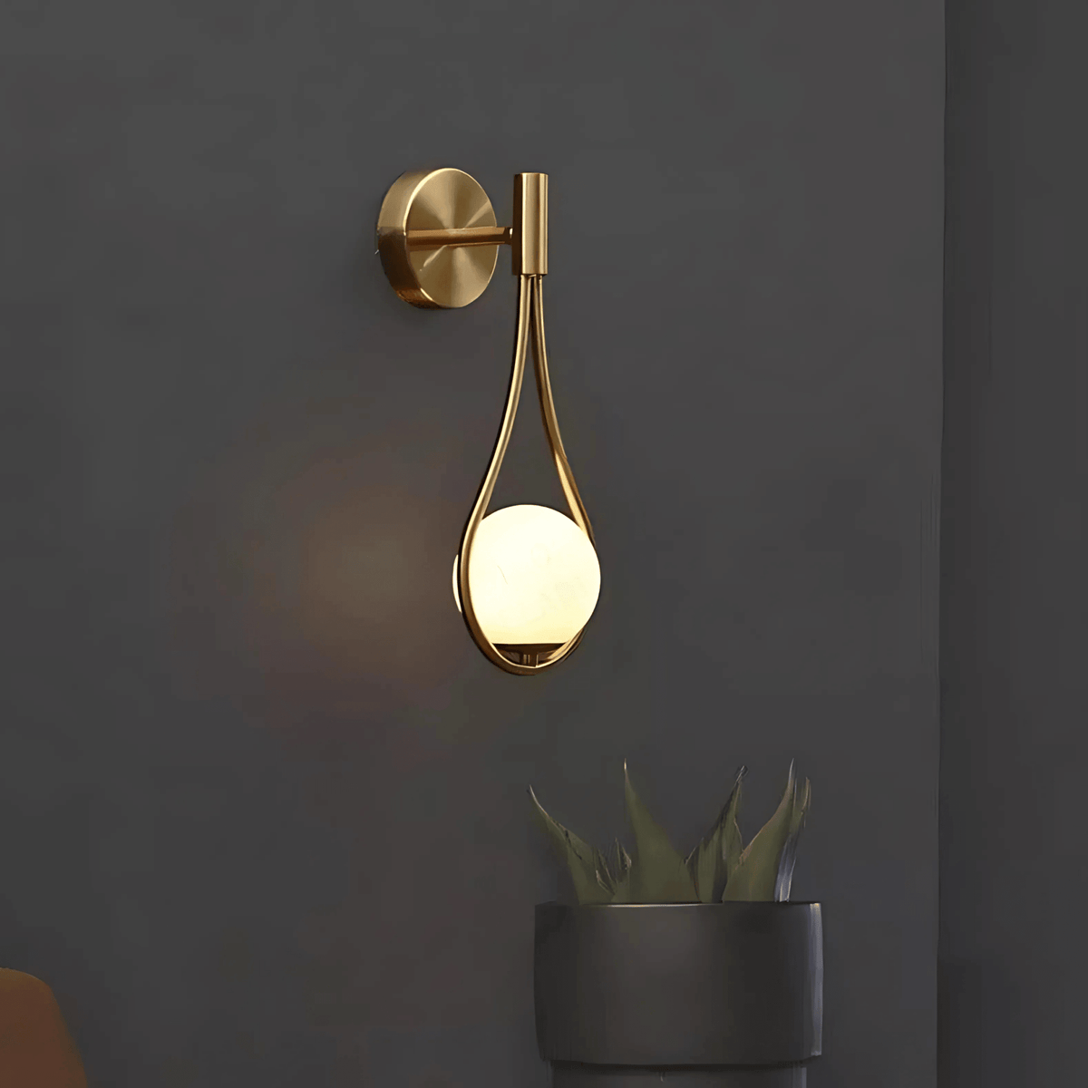 Brass globe wall sconce switched on against a dark gray wall
