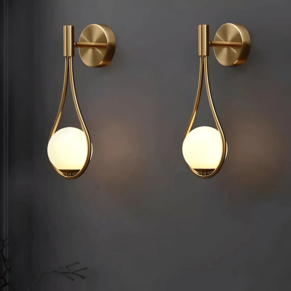 Pair of brass teardrop wall sconces lit on a dark wall