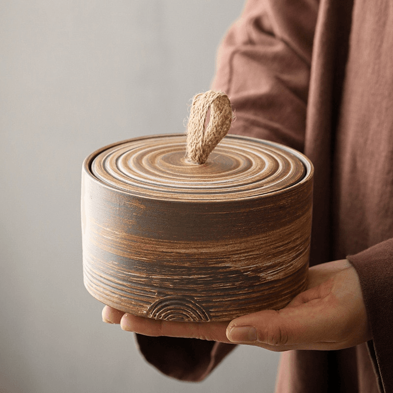 Handmade Japanese ceramic storage jar with hemp rope handle with the lid lifted to show the interior
