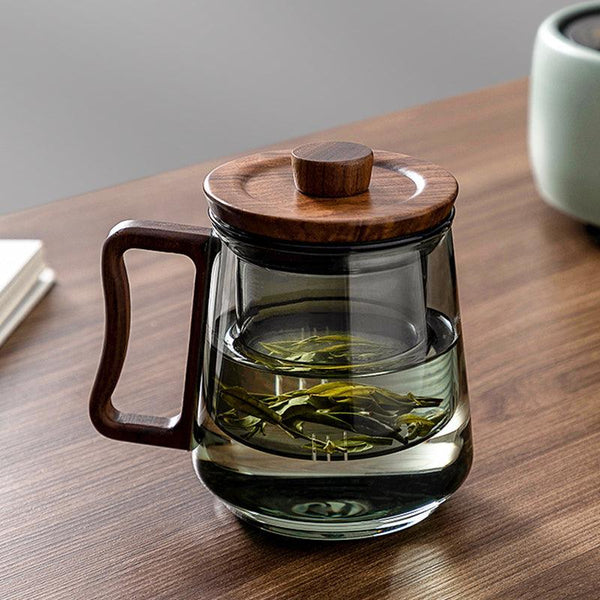 Heat resistant glass tea mug with wood lid and metal infuser on a light styled tabletop