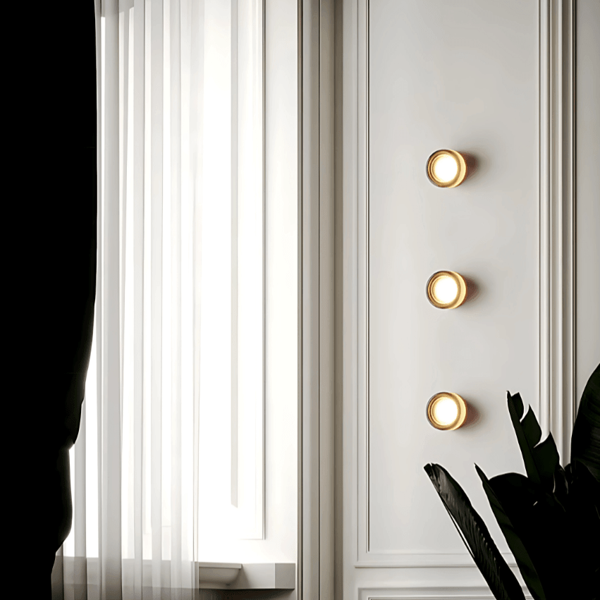Three Hera wall sconces in a column on a paneled wall beside a window