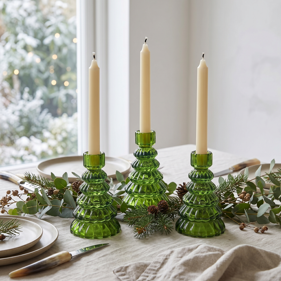 Three emerald glass tree candle holders lit with taper candles on a table