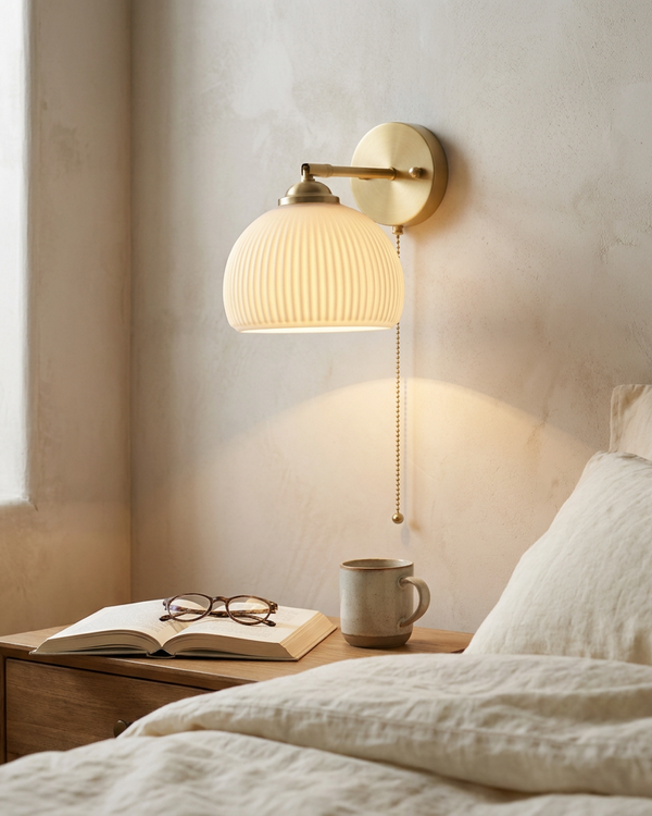 Lumen milk glass pull cord wall sconce glowing warmly on a bedroom wall above a nightstand