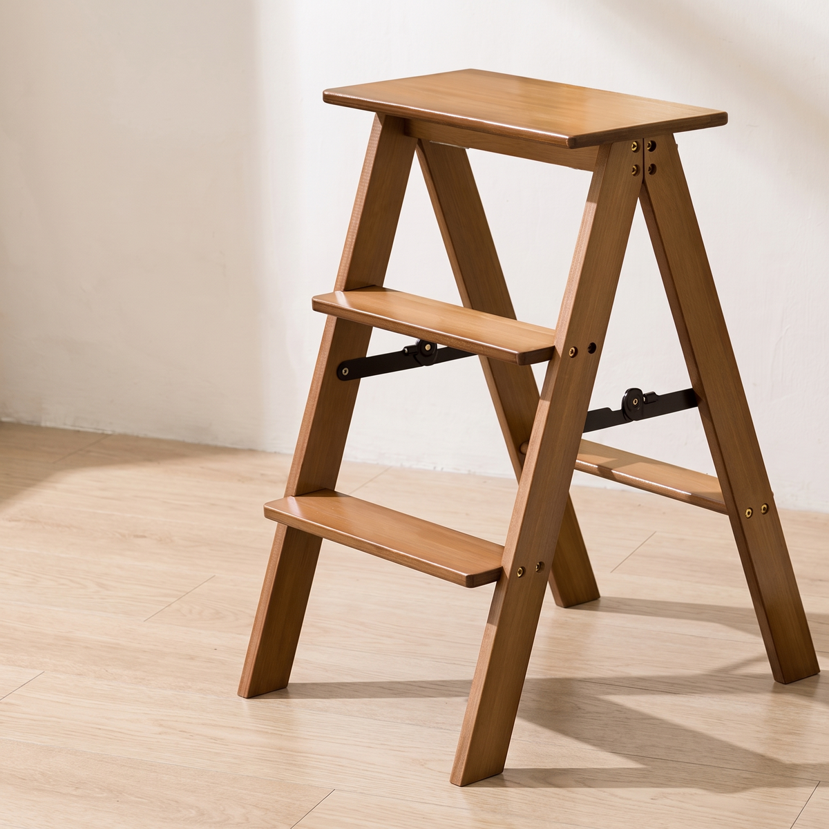 Bamboo three step folding stool with black metal braces on a wood floor