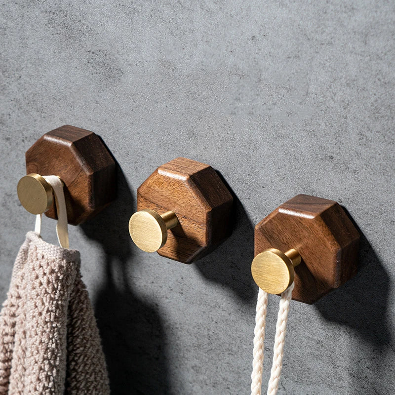 Row of three walnut hooks with brass pegs on a gray concrete wall