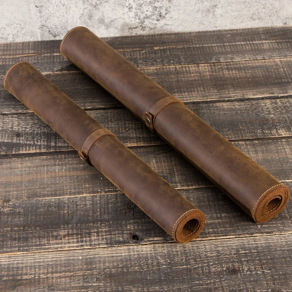 Two rolled brown leather desk mats on a rustic wood table
