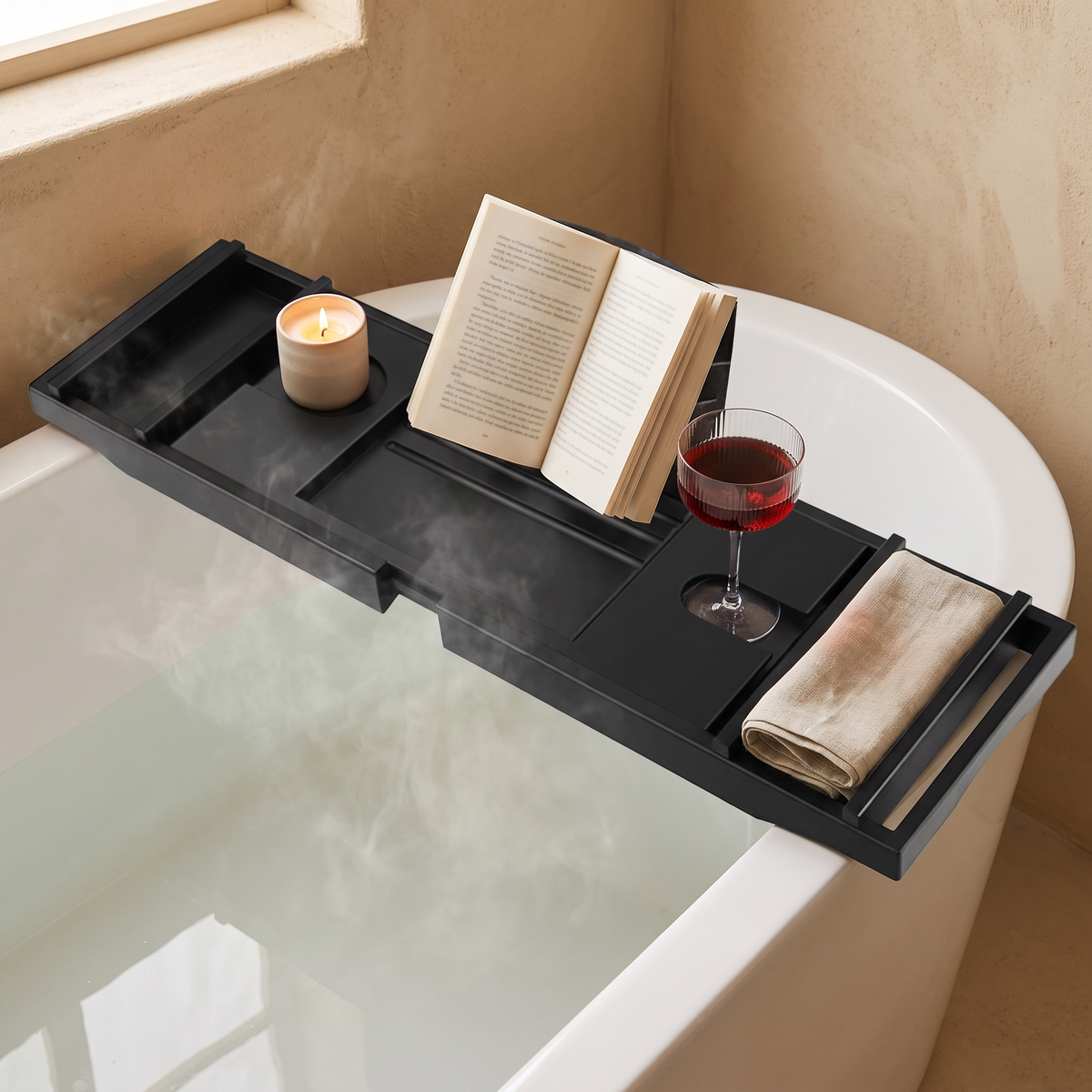 Black bamboo bath caddy across a tub with a book, candle and wine glass