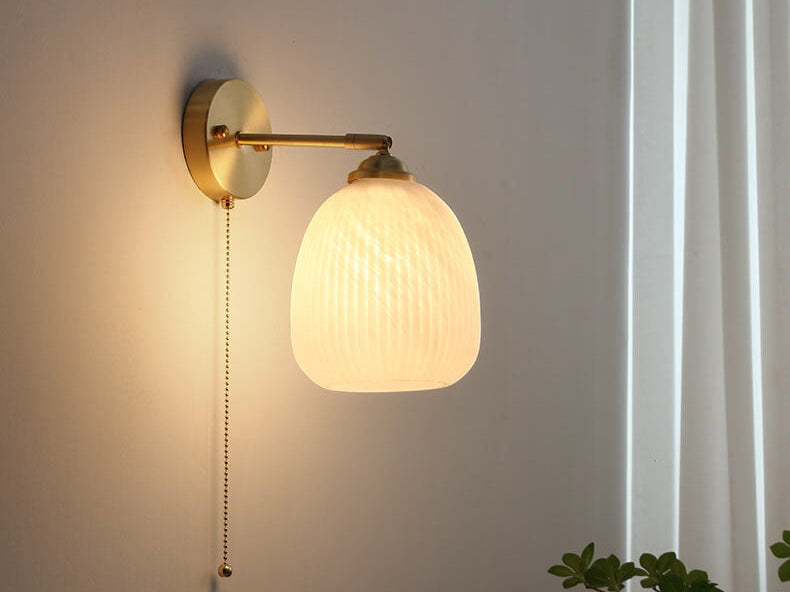Milk glass wall sconce with a brass arm and pull chain glowing on a white wall