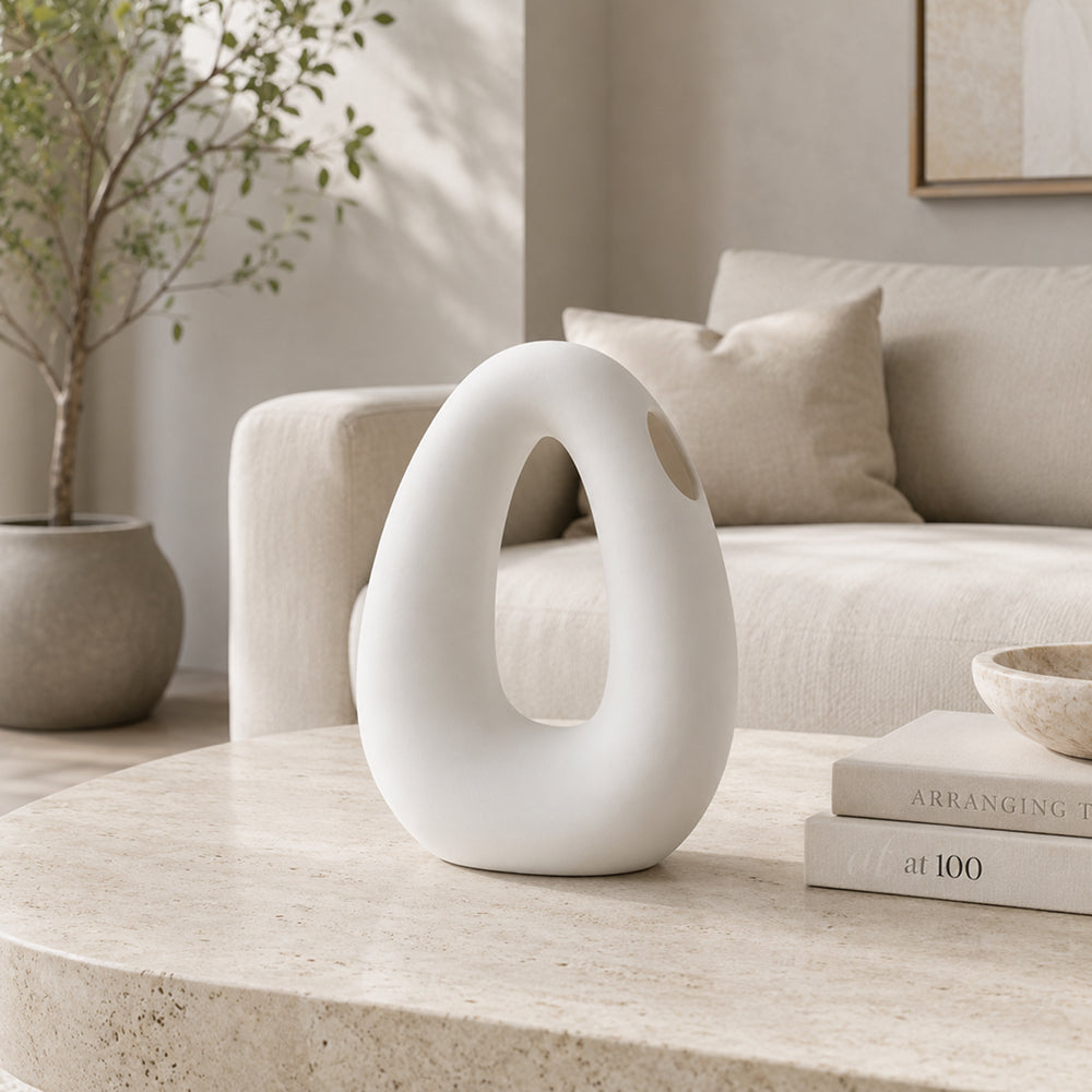 Beige oval ceramic vase with a cut out center on a console
