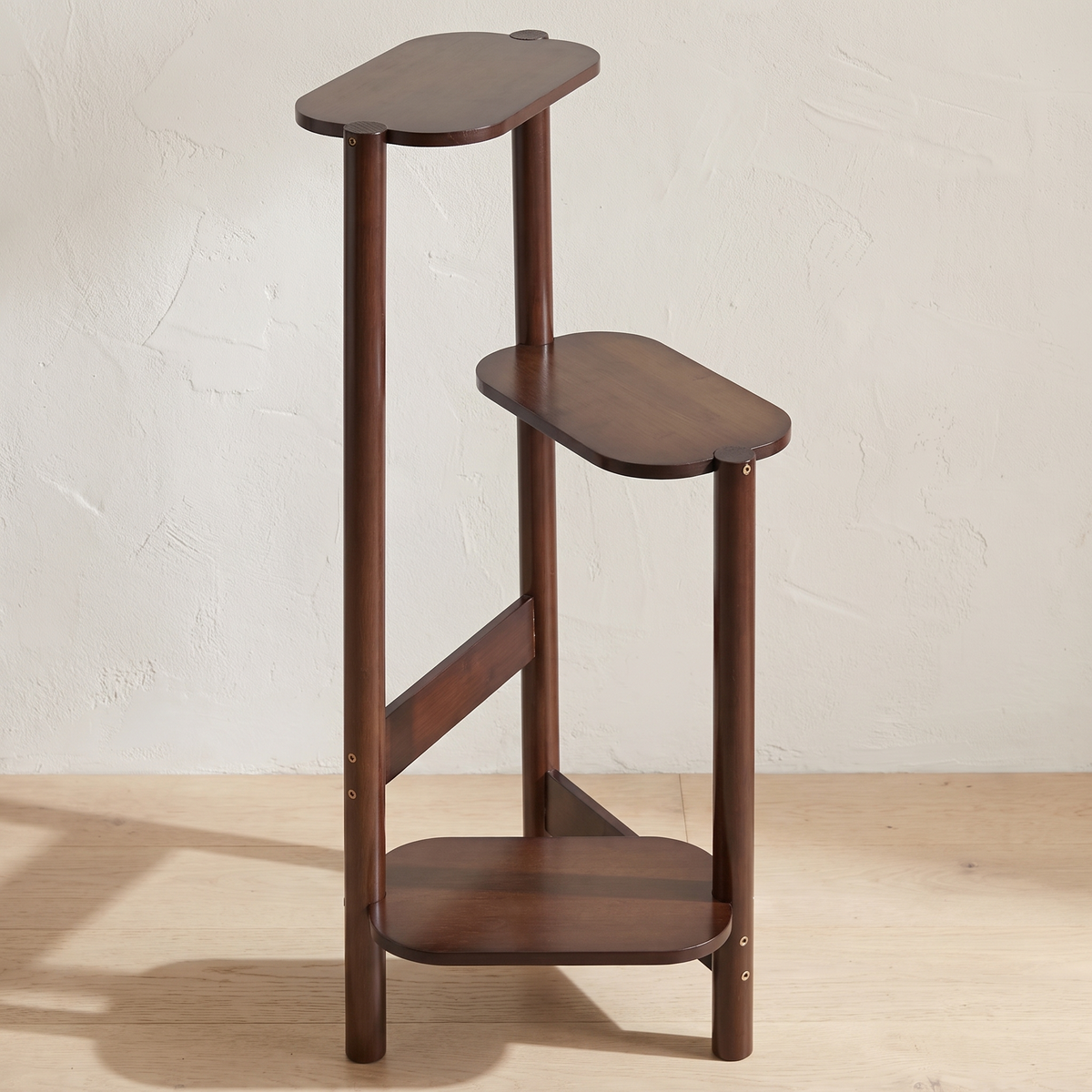 Dark brown bamboo plant stand with three stepped shelves on a wood floor