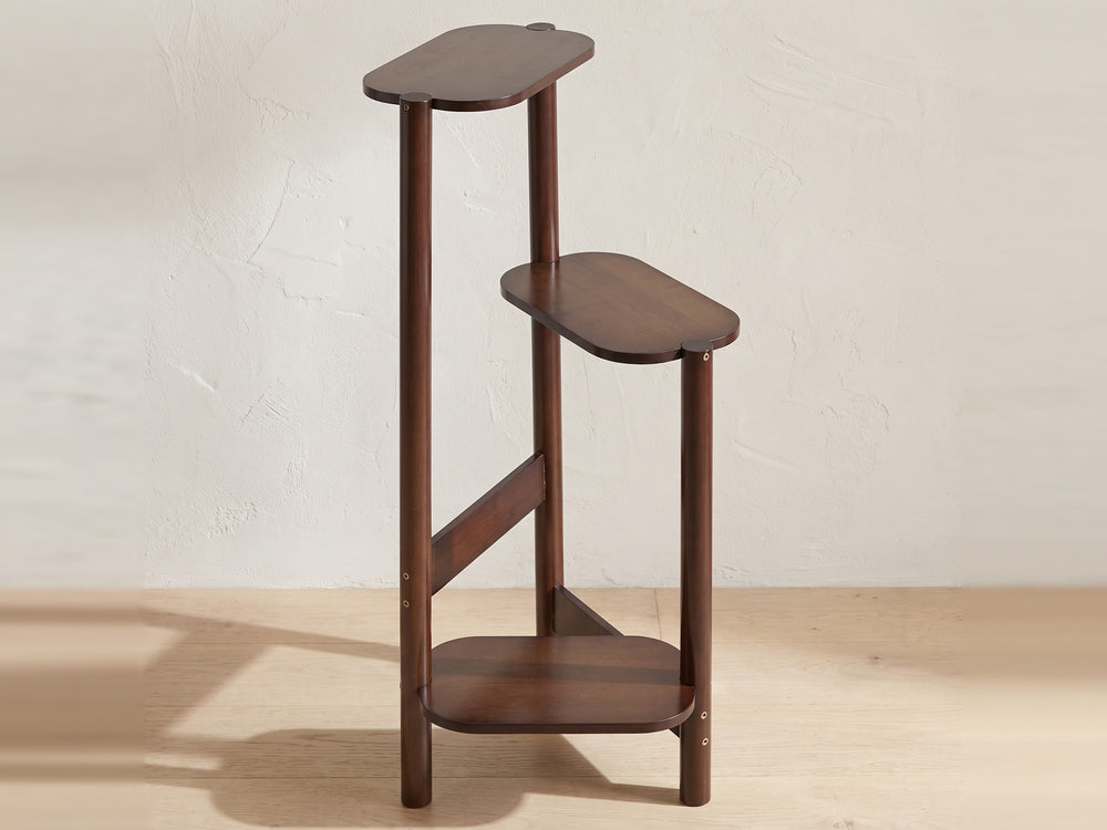 Dark brown bamboo plant stand with three stepped shelves on a wood floor