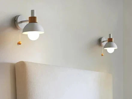 Two white wall sconces with wood rings and pull chains above a headboard
