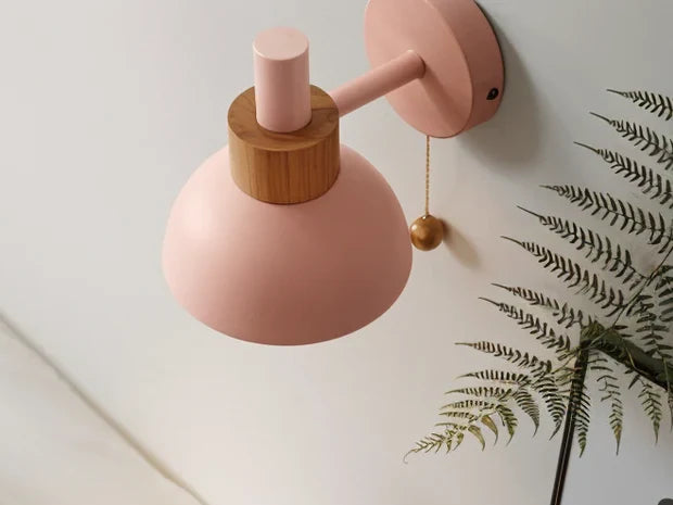 Pink wall sconce with a dome shade, wood collar and pull chain, seen from below