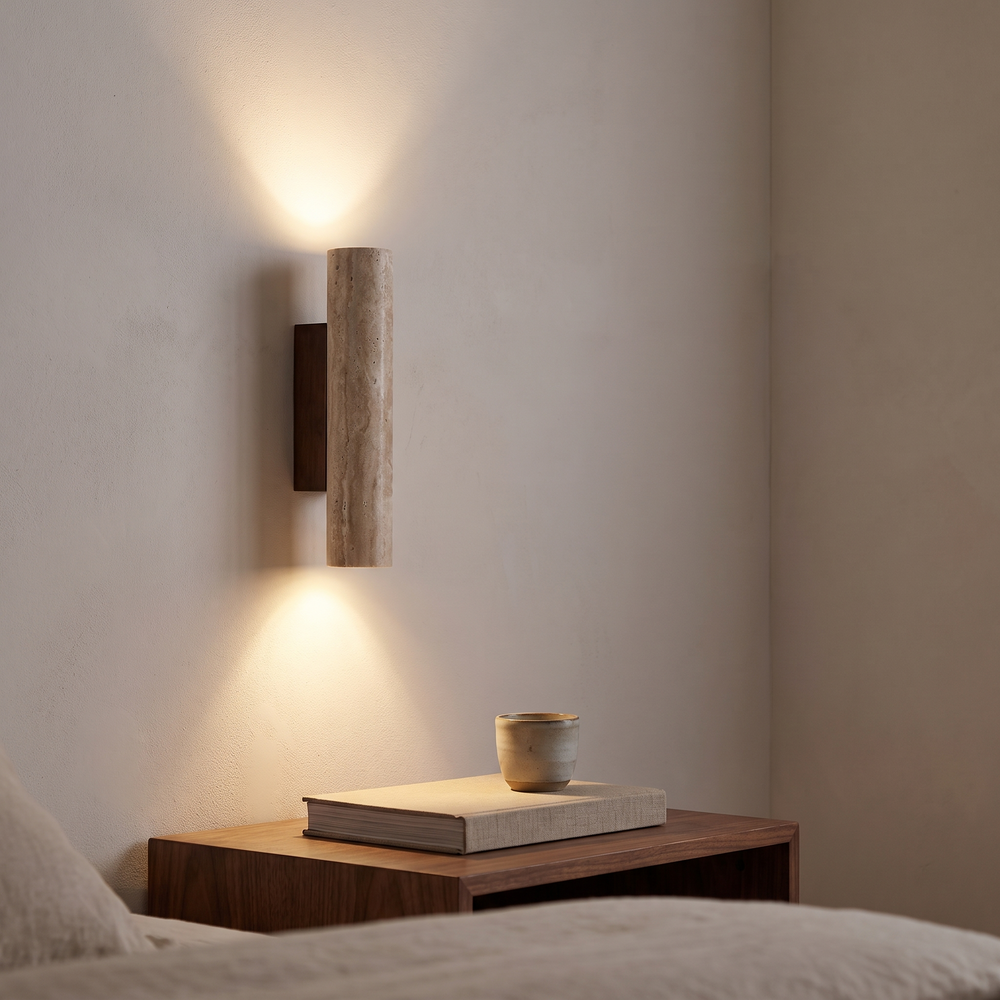 Travertine wall sconce mounted above a walnut nightstand in a bedroom, throwing a warm cone of light up and down the plaster wall