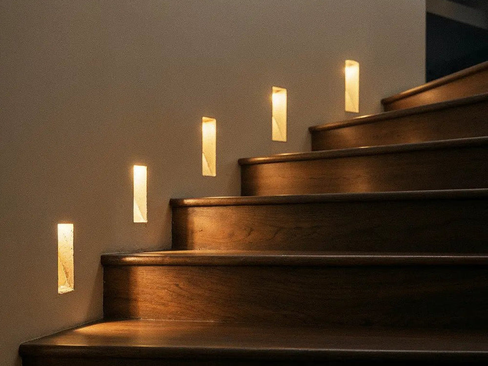 Recessed LED stair lights glowing along a wall beside wooden steps