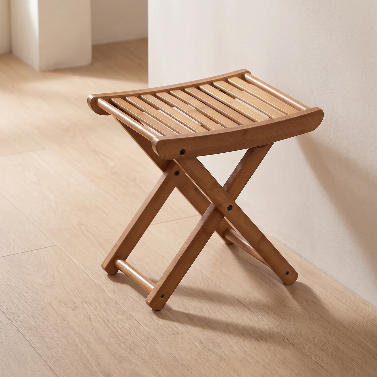 Brown bamboo folding stool standing on a wood floor against a white wall