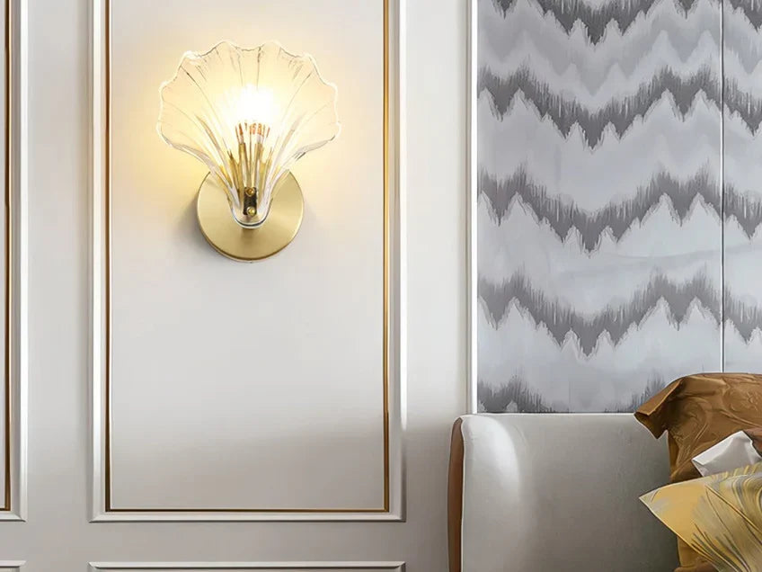 Clear glass seashell wall sconce lit on a bedroom wall beside the bed