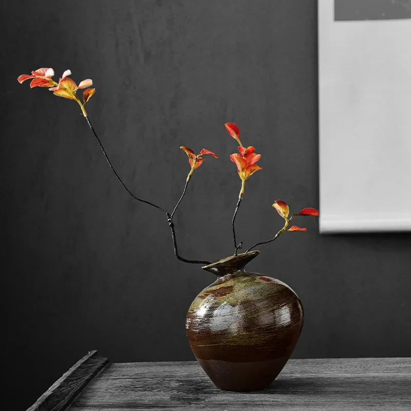 Green glaze bud vase with a single flowering branch against a dark wall
