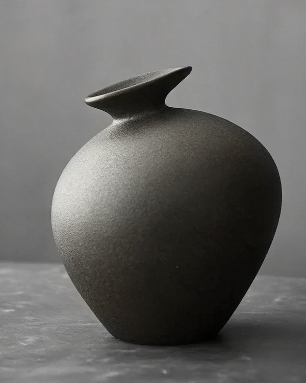 Matte black ceramic bud vase jar with a flared lip on a gray table