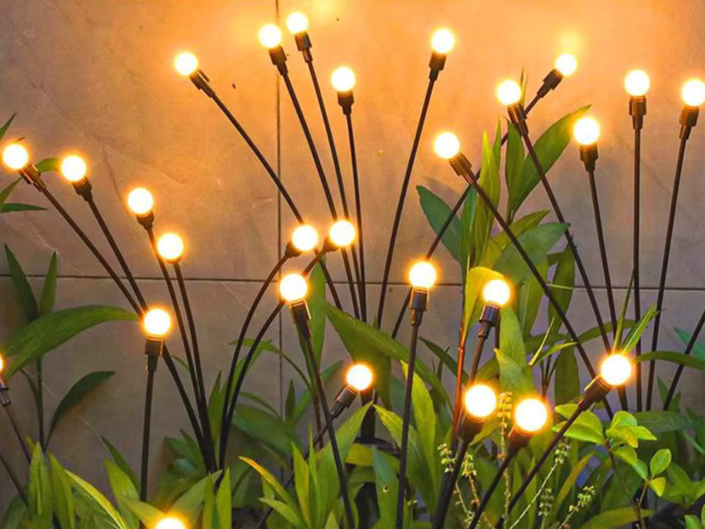 Solar firefly garden lights glowing among green plants in front of a garden wall at dusk