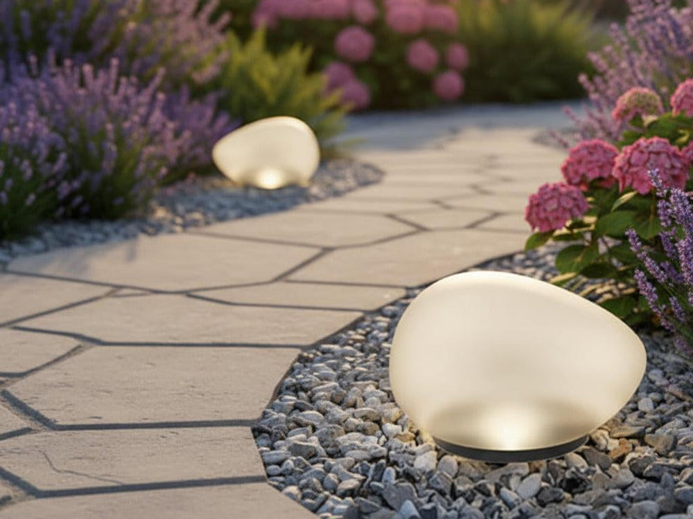 Two white pebble shaped solar lights on gravel beside a stone garden path